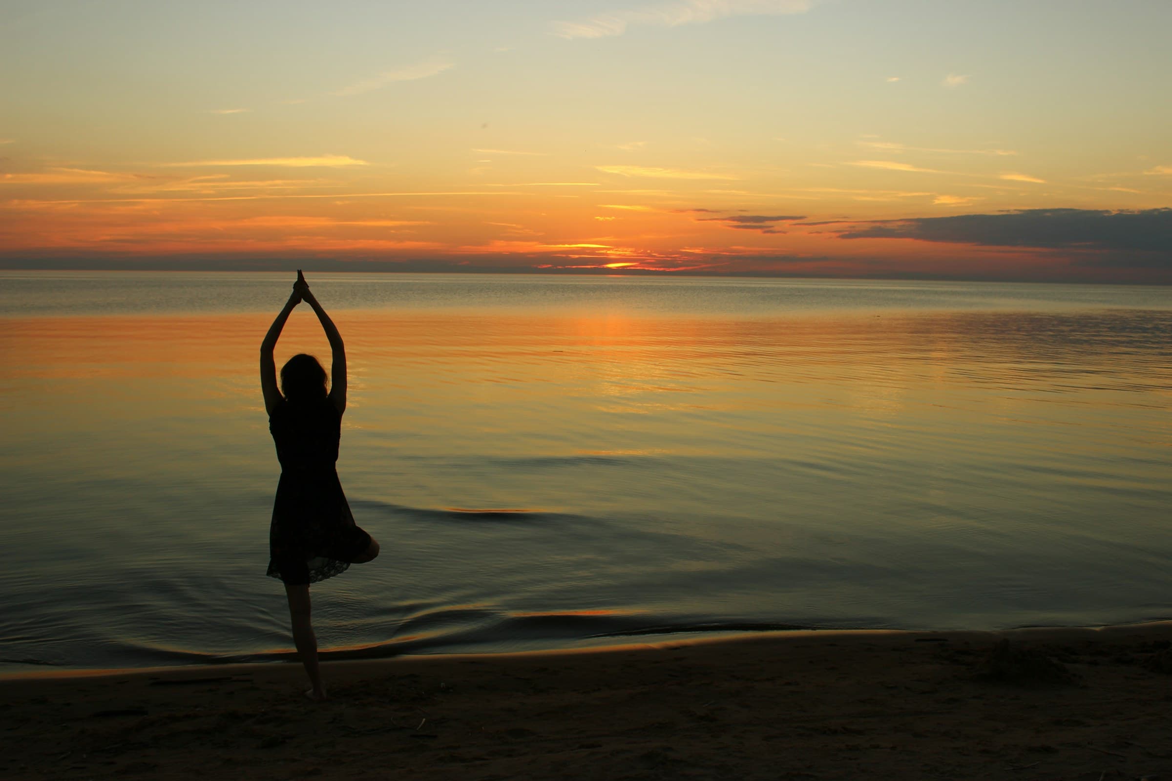 A yoga practitioner standing beside calm water at sunset