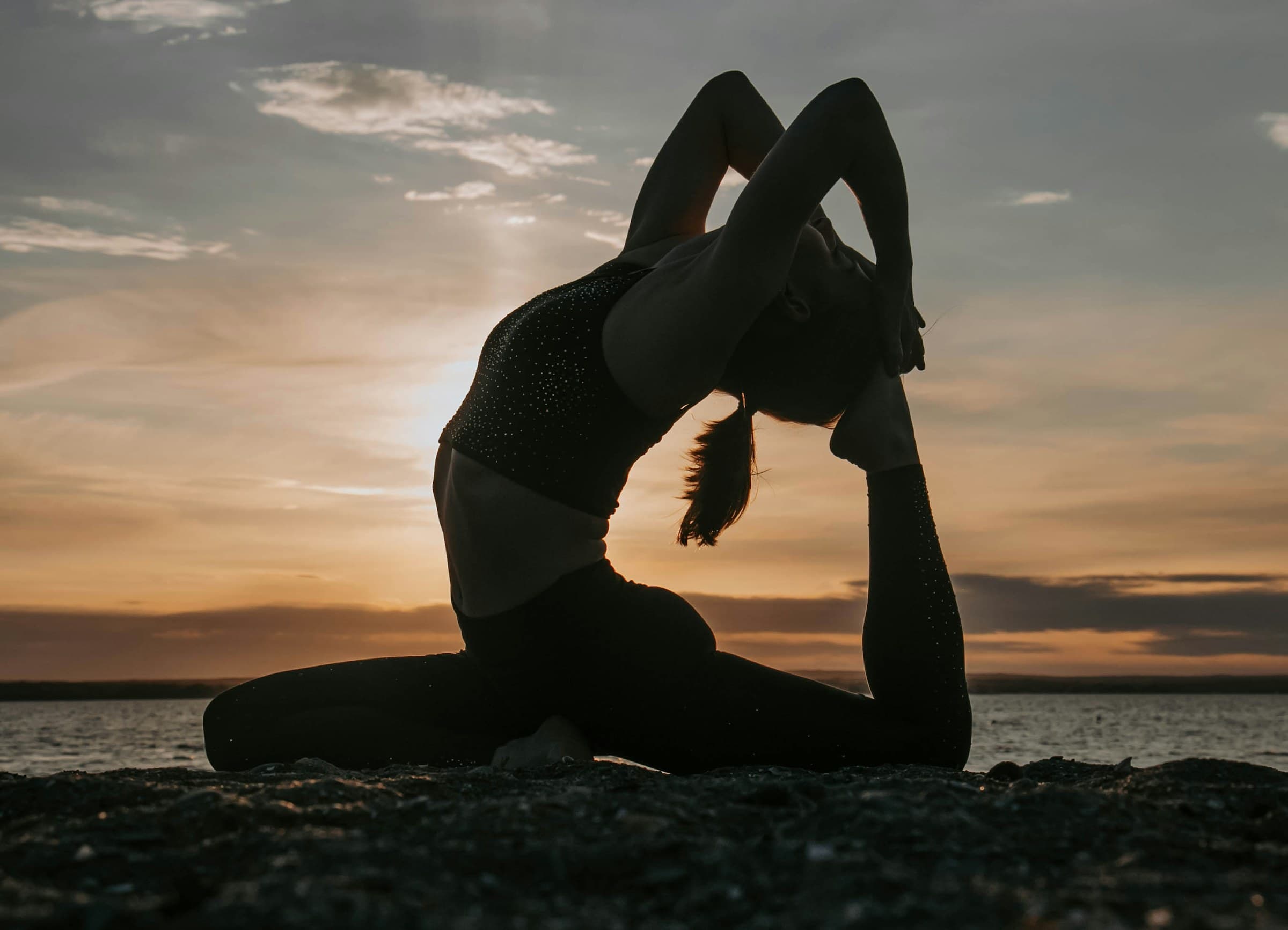 A yoga practitioner moving at sunset by the water